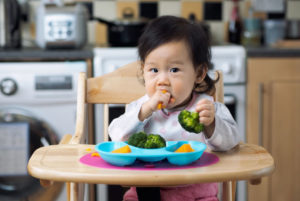 Baby in highchair eating broccoli
