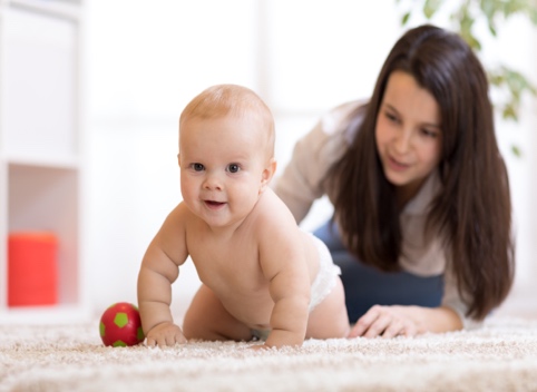 Baby crawling on ground with woman behind him encouraing