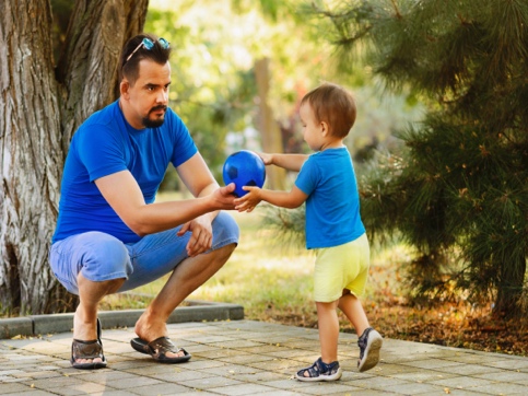 Man holding out a blue ball to young child
