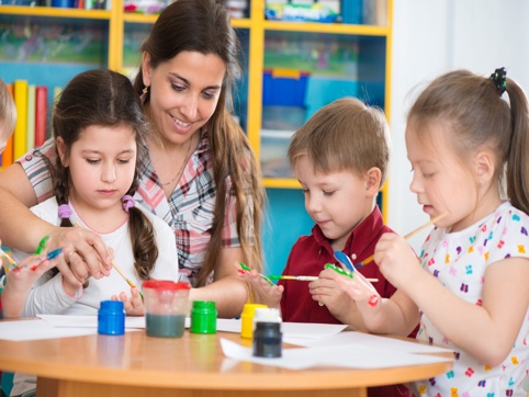 Woman helping children paint on paper