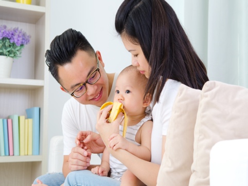 Mother and father helping baby eat a banana