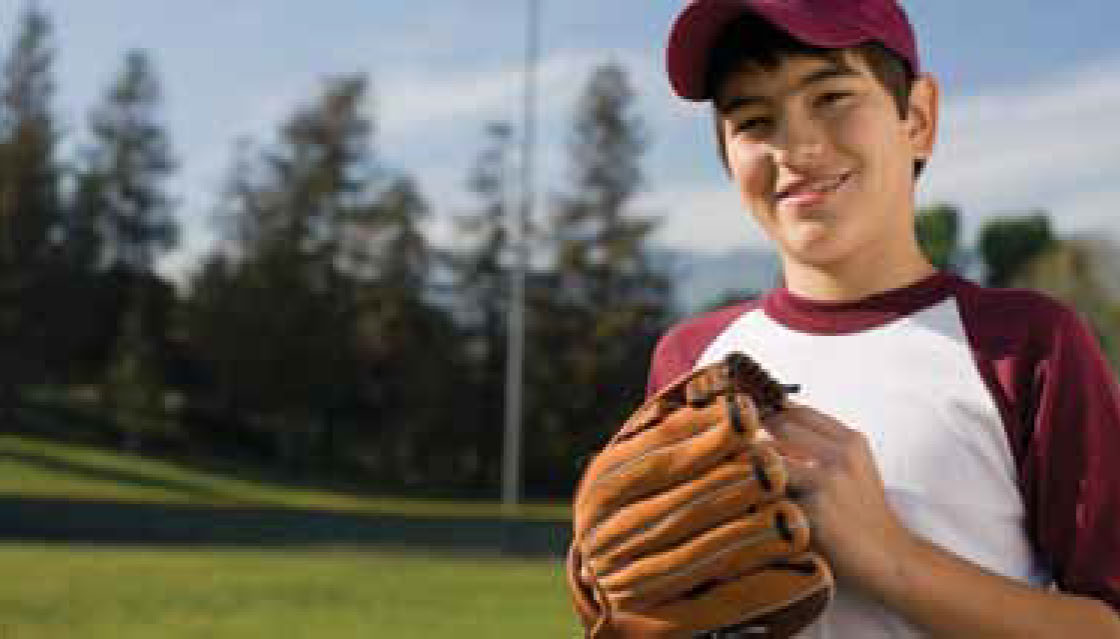 El muchacho sostiene el guante de béisbol en un campo y sonriendo.