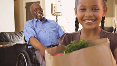 Chica sujetando comestibles para anciano en silla de ruedas
