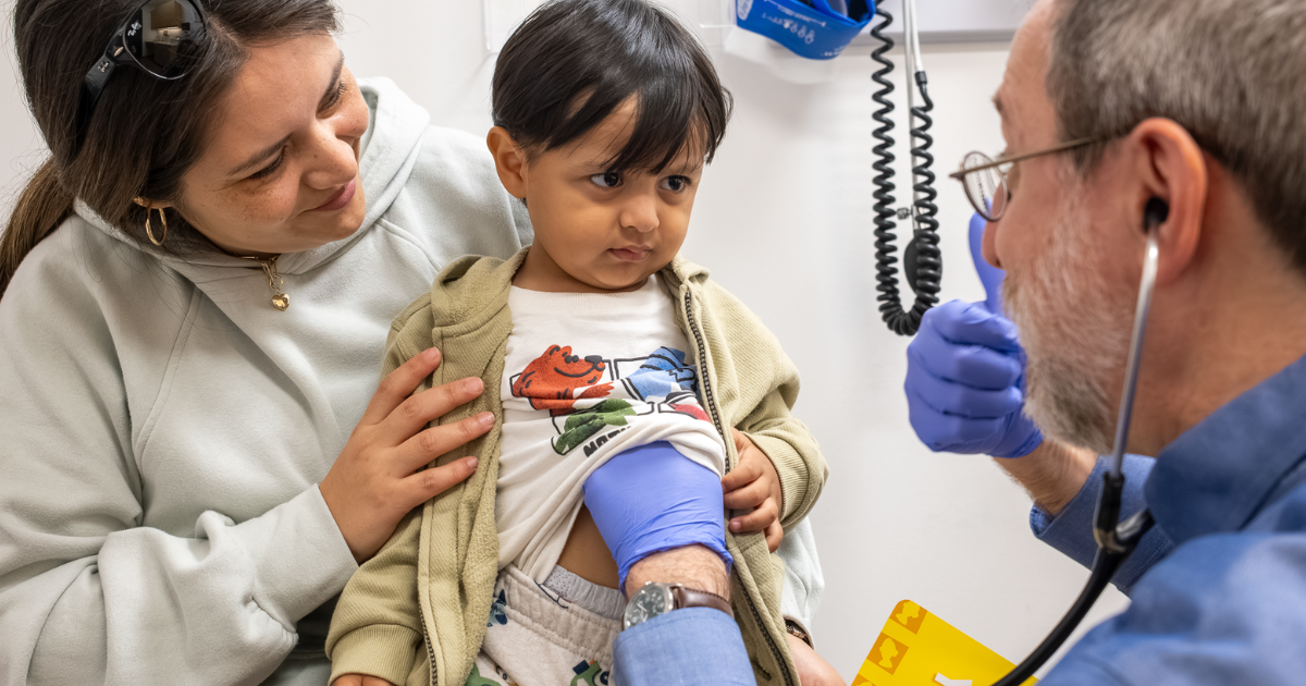 toddler being examined by doctor while sitting on moms lap toddler being examined by doctor while sitting on moms lap
